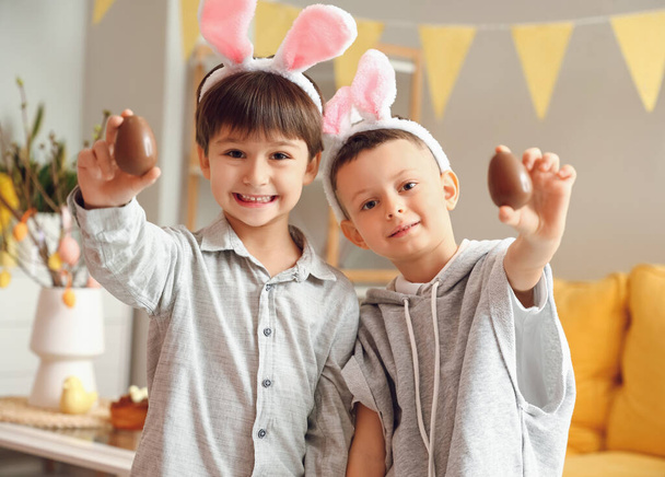 Lindos niños pequeños con orejas de conejo y huevos de Pascua de chocolate en casa - Foto, Imagen