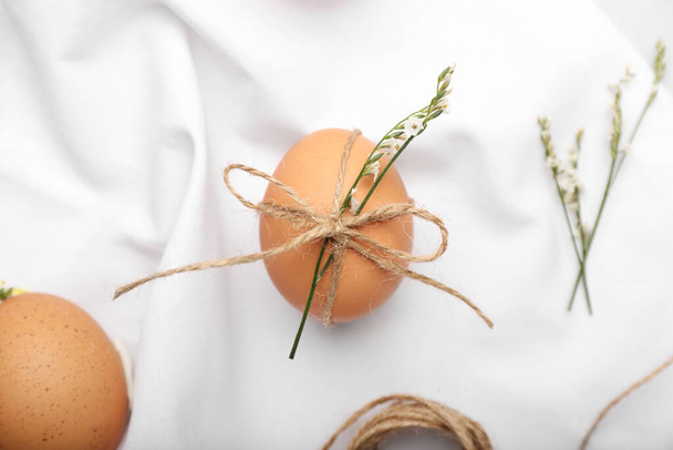 Пасхальные яйца, веревка и цветы на светлом фоне ткани - Фото, изображение