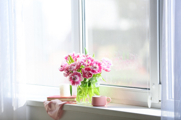 Wazon z pięknymi kwiatami tulipanów, filiżanka herbaty, książka i świeca na parapecie - Zdjęcie, obraz