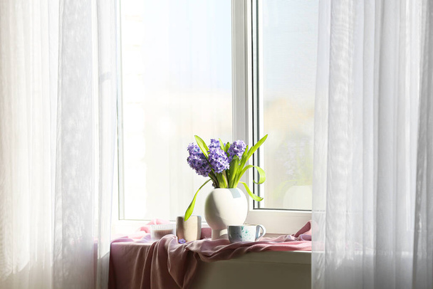美しいヒヤシンスの花、窓辺の紅茶とキャンドルの花瓶 - 写真・画像