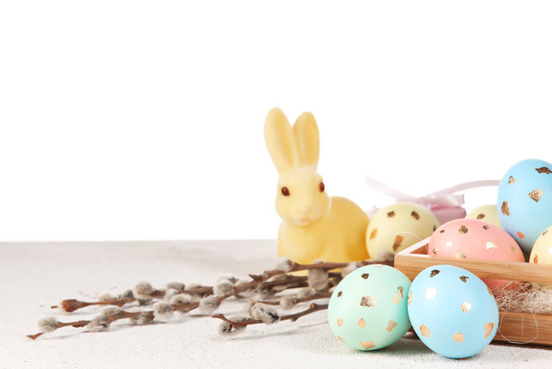 Scatola con uova di Pasqua dipinte, rami di salice e coniglietto sul tavolo su sfondo bianco - Foto, immagini