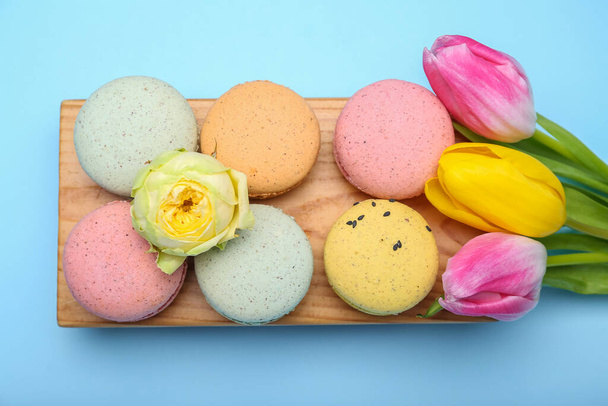 Puinen lauta maukkaita makaroneja ja kukkia värillinen tausta. Kansainvälinen naistenpäivä juhla - Valokuva, kuva