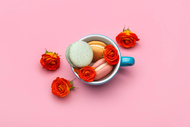 Cup with sweet macaroons and rose flowers on pink background. International Women's Day celebration - Foto, Bild