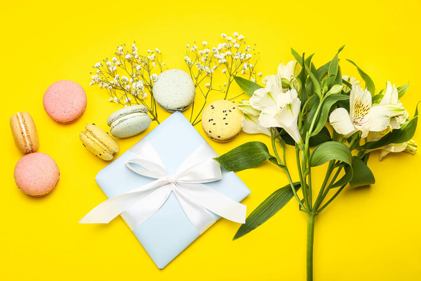 Composición con regalo para la celebración del Día Internacional de la Mujer, macarrones y flores sobre fondo amarillo - Foto, imagen