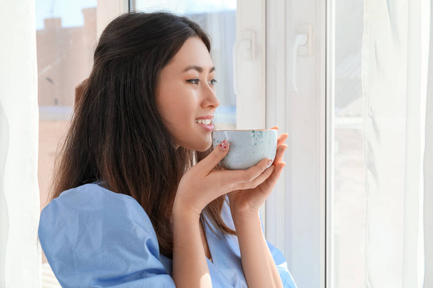 Hübsche junge Asiatin trinkt Kaffee am Fenster - Foto, Bild