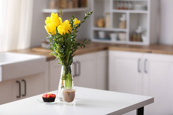 Vase with flowers, muffin and cup of coffee on dining table in kitchen - Фото, зображення