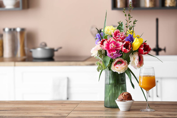 Jarrón con flores, magdalena y vaso de jugo en el mostrador de cocina de madera - Foto, Imagen