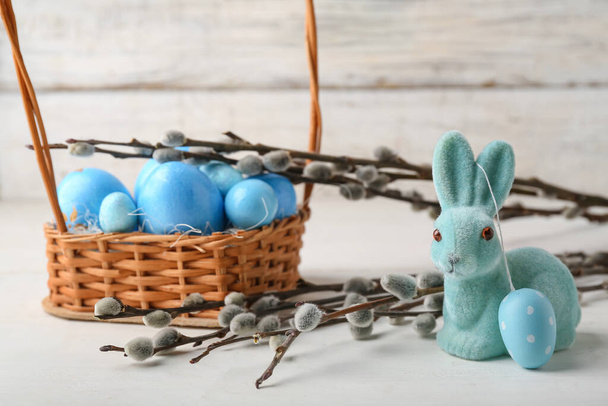Willow branches, bunny and basket with painted Easter eggs on light wooden background - Foto, imagen