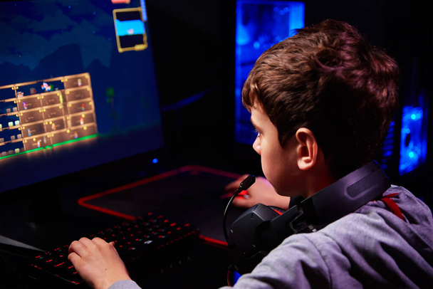 Teenager chlapec hrát počítačové videohry v tmavé místnosti, používat neonové barvy rgb mechanické klávesnice, pracoviště pro počítačové hry, dětské herní závislosti - Fotografie, Obrázek