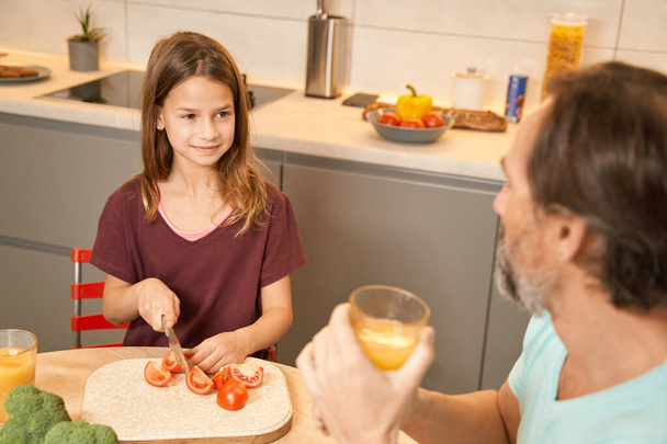 Adolescente préparant des légumes à côté de son père dans la cuisine - Photo, image