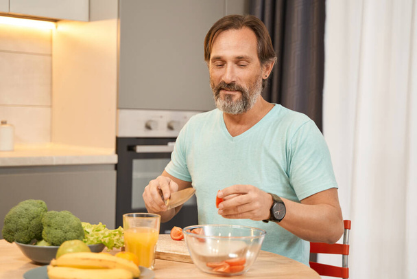 Бородатий дорослий чоловік сидить за кухонним столом
 - Фото, зображення