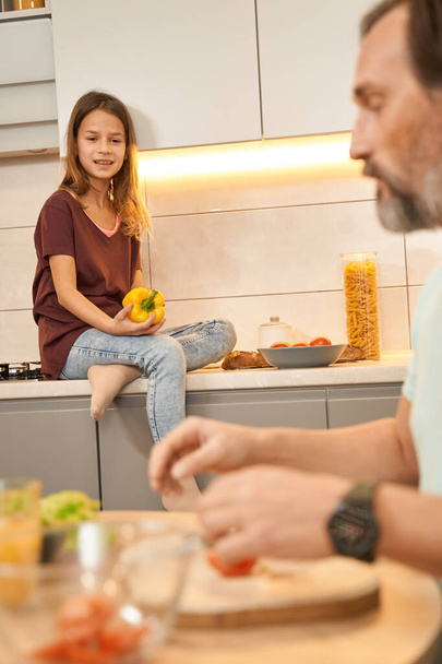 Teen girl is sitting while her father is cooking salad - Foto, immagini
