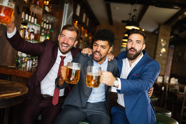 Business men fans screaming and watching football on TV and drink beer in a pub - Foto, imagen