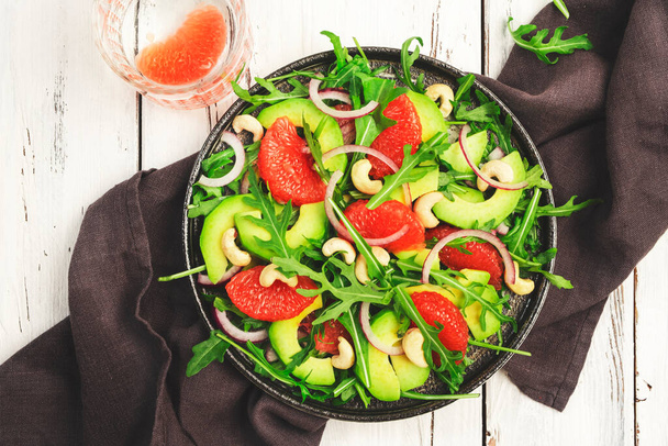 Healthy vegan vegetarian lunch salad with arugula, avocado, grapefruit and cashews and dressing of olive oil, honey and wine vinegar. White rustic kitchen table, top view - Photo, image