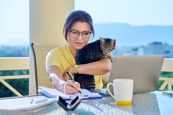 Home workplace female freelancer working remotely with pet cat in her arms - Zdjęcie, obraz