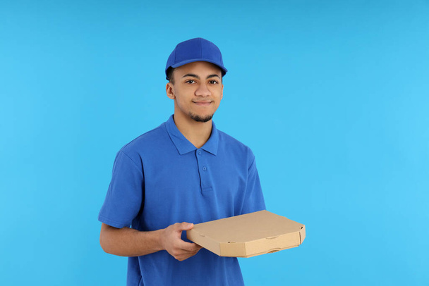 Młody dostawca w czapce na niebieskim tle - Zdjęcie, obraz