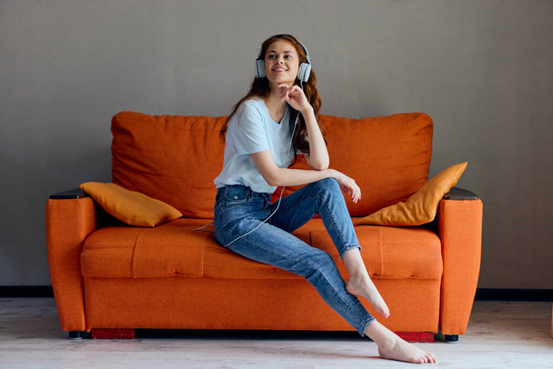 ritratto di una donna sul divano arancione che ascolta musica con le cuffie. Foto di alta qualità - Foto, immagini