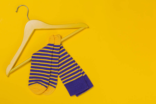 pair of blue yellow striped socks on a yellow wooden hanger, shopping and discounts concept, on yellow background - Foto, afbeelding