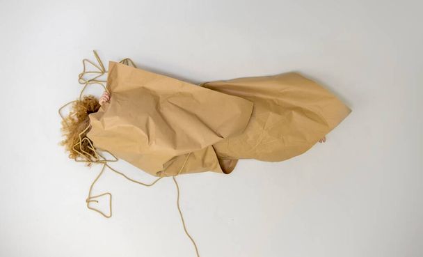 mujer pelirroja rubia rizada casi completamente cubierta envuelta en papel de envolver y cuerda, como paquete de regalo, espacio para copiar - Foto, imagen