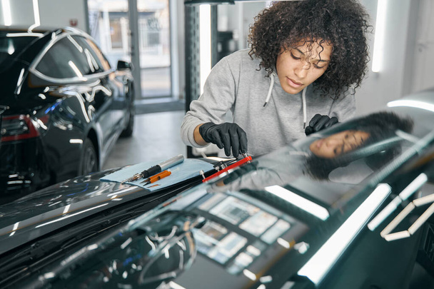 Concentrated car mechanic affixing automotive equipment to windscreen - Photo, image