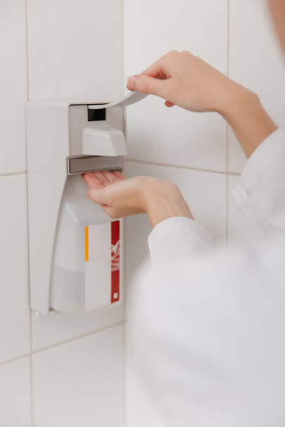 The doctor in white uniform disinfects his hands. Surgeon washing hands hospital concept. The nurse washes her hands with sanitizer or dispenser or alcohol solution for hand disinfection, close-up - Fotoğraf, Görsel