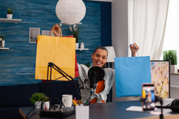 Twórczyni treści kobiecych pokazująca kolorowe papierowe torby na prezent online. - Zdjęcie, obraz