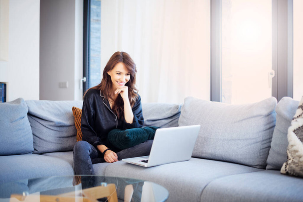 Candid shot of happy woman using her laptop while relaxing on the sofa at home. - Fotoğraf, Görsel