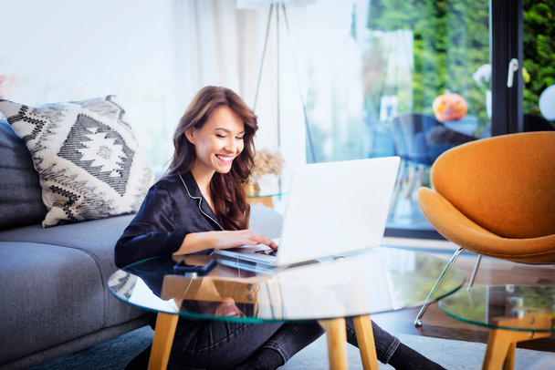 Shot of happy woman sitting on the floor at home and using her laptop. - Foto, Bild