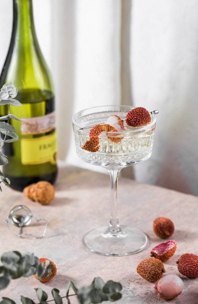 Koud vers geperste lychee cocktail met champagne en vers fruit op een licht grijze betonnen achtergrond. Selectieve focus, kopieerruimte. - Foto, afbeelding