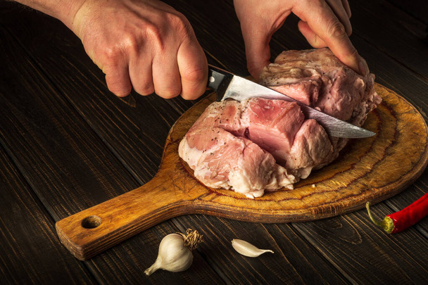 The chef cuts meat with a knife before baking. Spices on the kitchen table in a restaurant for preparing a delicious lunch or dinner - Photo, Image
