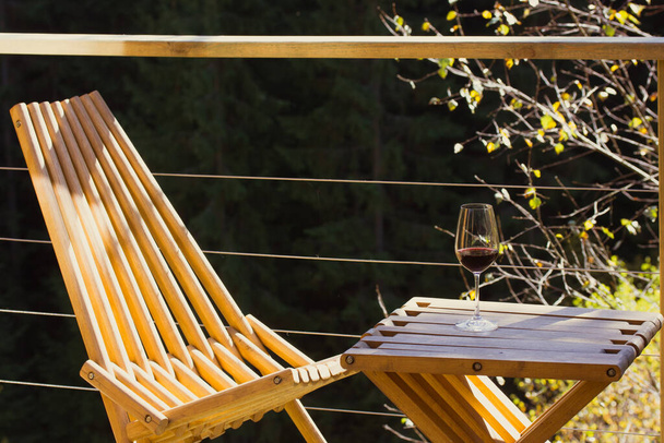 Mobília de jardim dobrável de madeira - uma mesa e cadeira - em pé na varanda do terraço em madeiras verdes. Um copo de vinho tinto está na mesa. Relaxar ao ar livre em um com a natureza no outono. Casa na floresta.  - Foto, Imagem