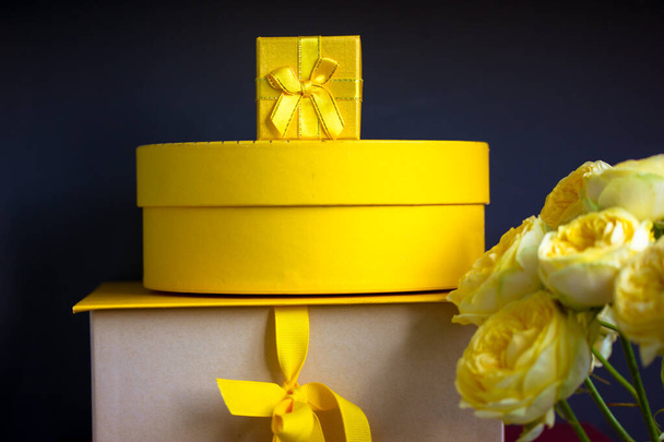 Un montón de cajas de regalo amarillas apiladas sobre fondo gris oscuro negro, ramo de rosas amarillas de Austin. Tarjeta de felicitaciones con regalos para cumpleaños, Día de la Madre, aniversario. Compras, ventas, regalos. - Foto, Imagen