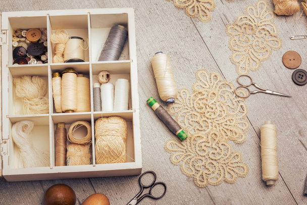 Set naaibenodigdheden op een grijze tafel: naaigaren, knopen, grijze doek, witte doos. Vintage of retro effect. Horizontaal. - Foto, afbeelding