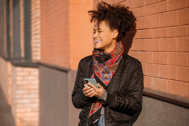 Chica joven de pelo oscuro en chaqueta con un teléfono en las manos - Foto, Imagen