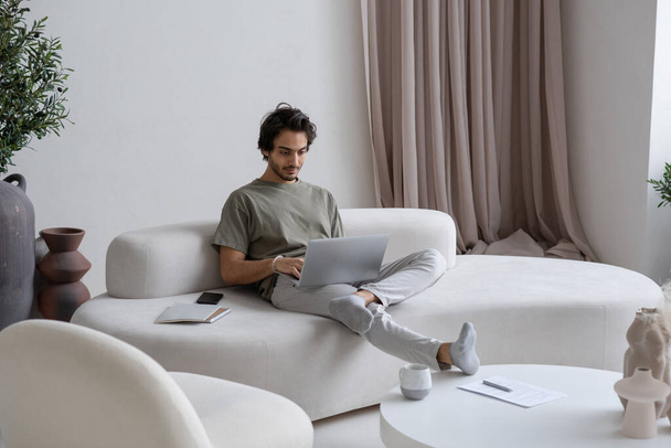 Jovem funcionário do sexo masculino em casualwear sentado no sofá e digitação - Foto, Imagem