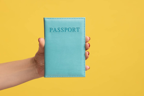 Closeup side view of woman hand holding blue passport, traveling abroad, visa and green card receiving, legal immigration. Indoor studio shot isolated on yellow background. - Photo, image