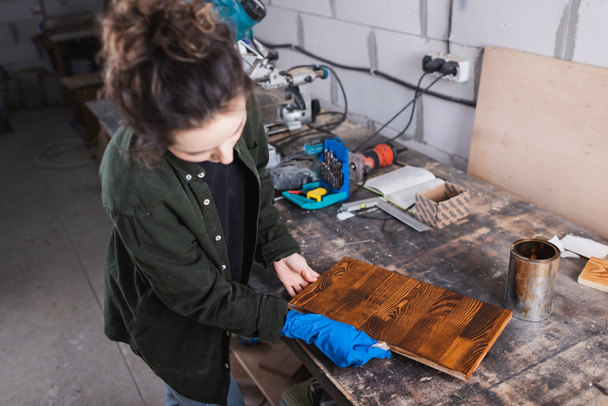 Carpintero aplicando mancha de madera sobre tabla en taller  - Foto, Imagen