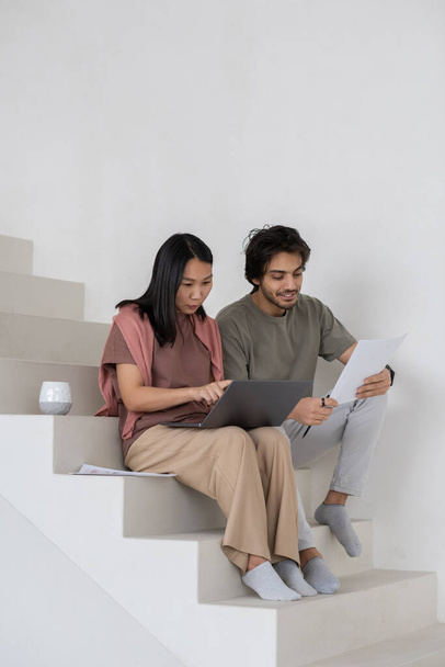 Happy young businessman with document sitting by female colleague with laptop - Photo, Image