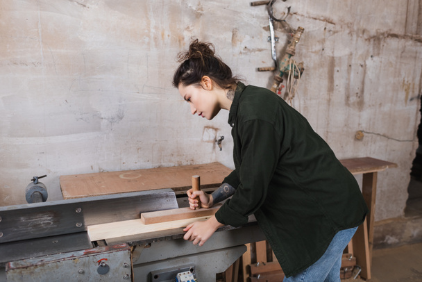 Seitenansicht des Tischlers bei der Arbeit mit Planke und Tischler in der Werkstatt  - Foto, Bild