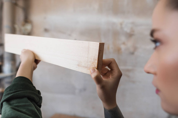 Θολή σχεδιαστής επίπλων κρατώντας ξύλινη σανίδα στο εργαστήριο  - Φωτογραφία, εικόνα