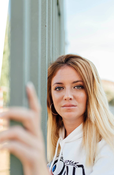 Portrait of blonde woman leaning head on a fence and touching it with hand - Photo, image
