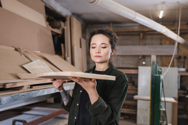 Jeune menuisier tenant une planche de bois floue dans l'atelier  - Photo, image