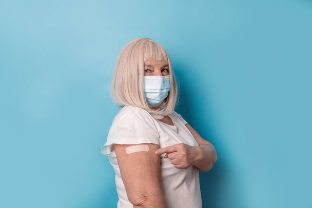 Vaccin en bejaarde mensen inenten. Gezond volwassen oudere oudere vijftiger jaren vrouw in beschermende medische masker met arm met gips na vaccin - Foto, afbeelding