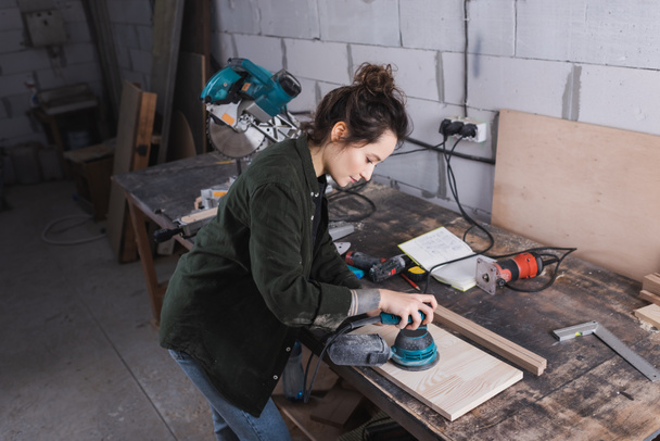 Vista lateral del tablero de lijado de carpintero cerca de herramientas y sierra de inglete en el taller  - Foto, imagen