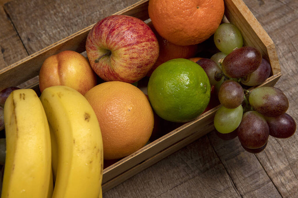 Caixa de madeira com frutas variadas, em tons quentes, vista de cima
 - Foto, Imagem