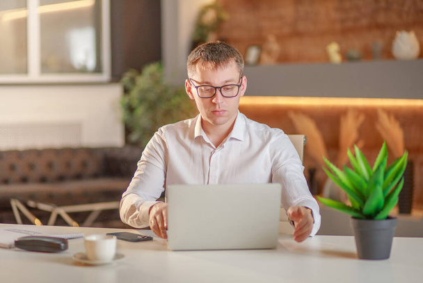 Бізнесмен сидить в офісі за великим столом перед ноутбуком і працює онлайн, відео чат, зв'язок між робочими моментами в Інтернеті, робота з офісу, концепція віддаленої роботи.. - Фото, зображення
