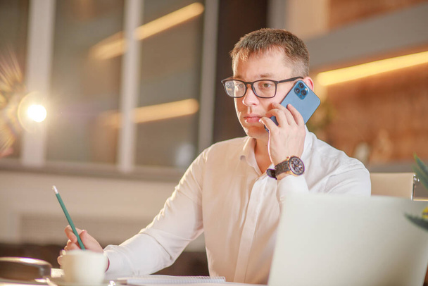 Biznesmen odbierający telefon siedzący przy biurku przed laptopem, łatwa bankowość internetowa, klient konsultujący menedżera telefonicznie o udanych negocjacjach mobilnych z klientem. - Zdjęcie, obraz