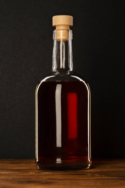 A bottle of alcohol with a cork on a wooden table and a dark background. - Foto, imagen
