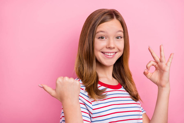 Photo of cool little blond girl index empty space show okey wear red t-shirt isolated on pink color background - Zdjęcie, obraz