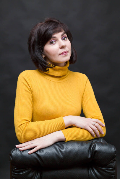 Woman in a yellow sweater, office manager near a leather chair. - Foto, immagini